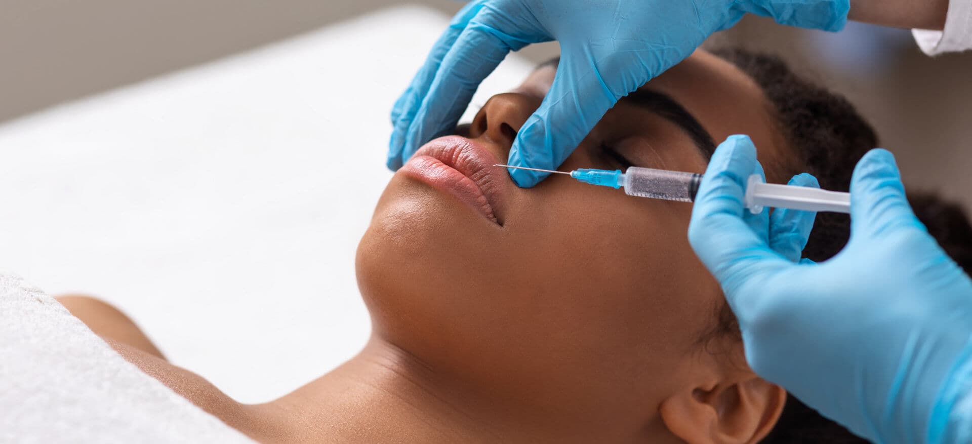 Black lady getting lip filling injection at modern beauty salon